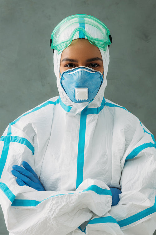 Female nurse wearing protective medical suit standing with arms crossed and looking at camera