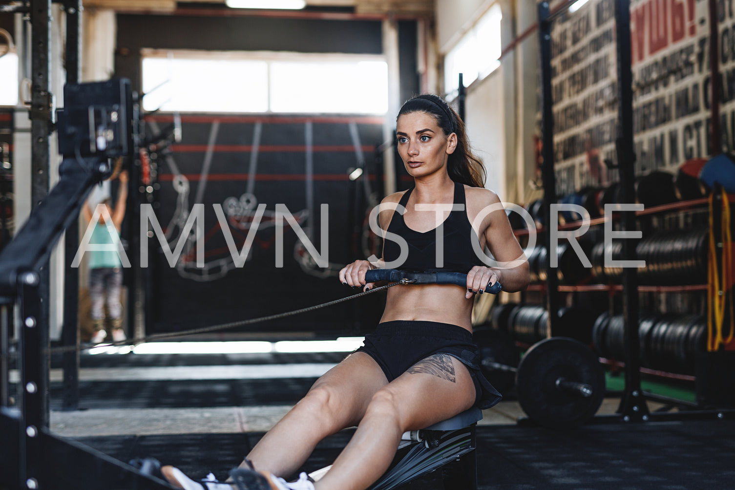 Muscular female using rowing machine in fitness club, front view	