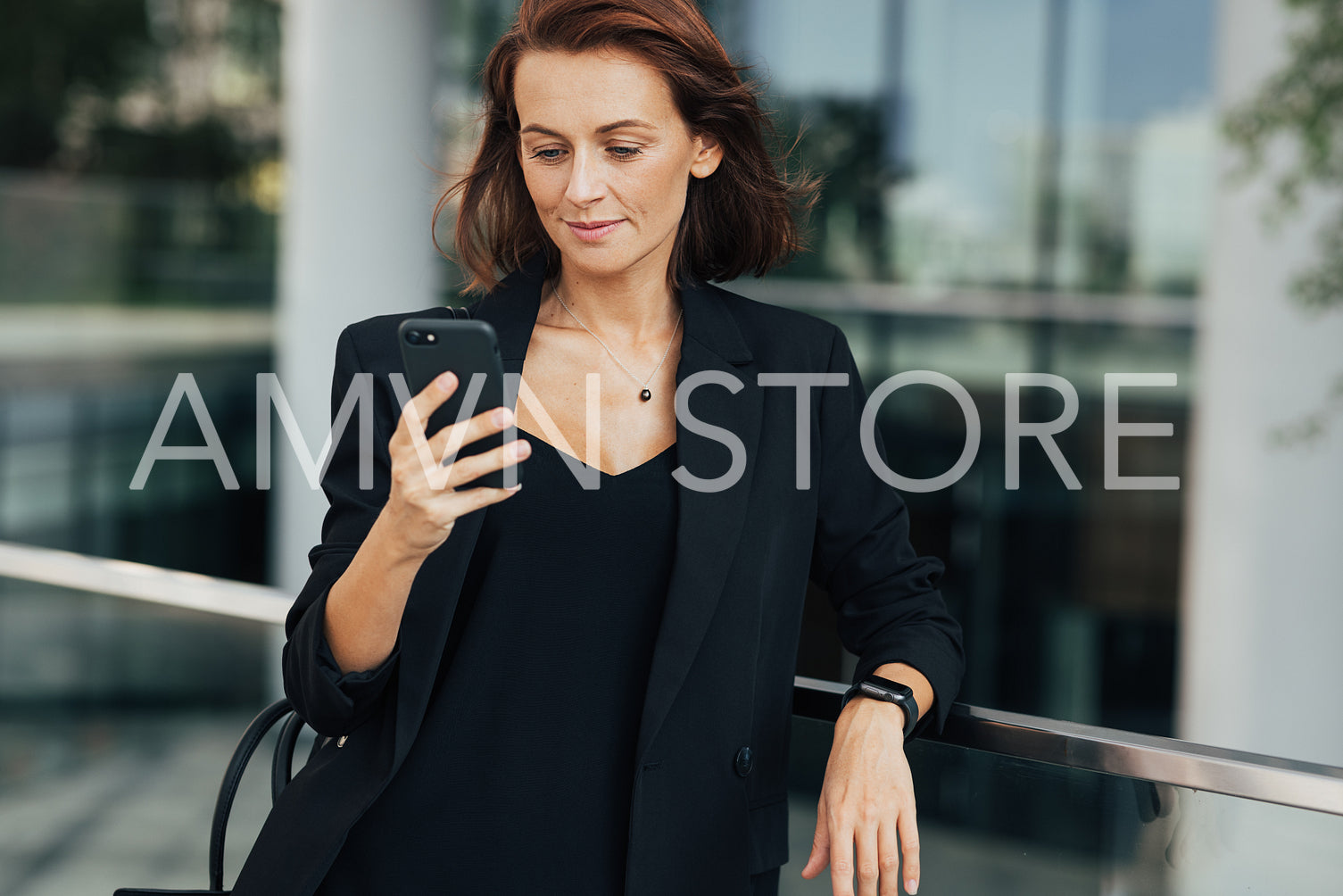 Confident middle-aged businesswoman standing outdoors and looking at a smartphone