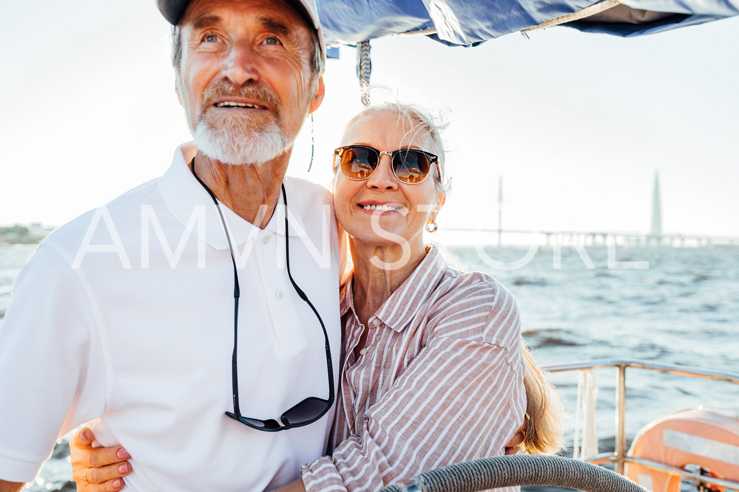 Two mature people standing on sailboat at steering wheel and embracing each other	