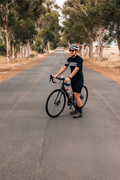 Young woman in sportswear standing on an empty road with bicycle