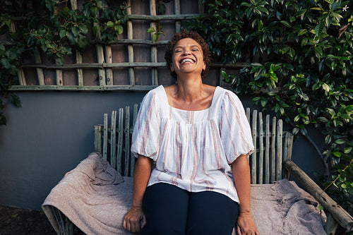 Middle aged woman laughing while sitting on a bench outdoors at backyard