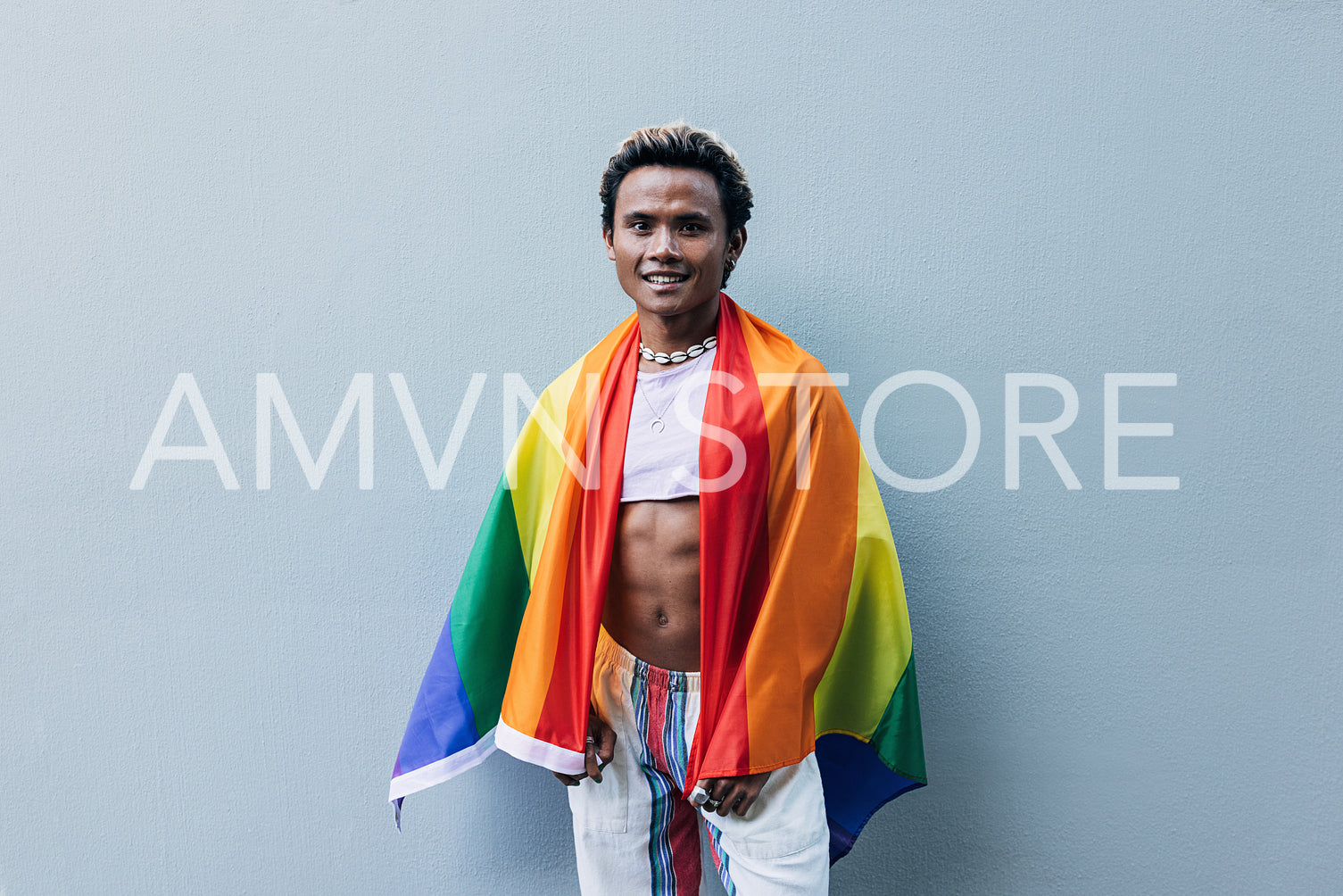 Young smiling male with LGBT flag at grey wall