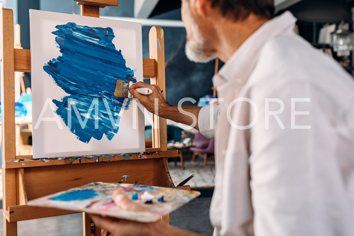 Inspired artist drawing an abstract picture in his workshop holding a palette	