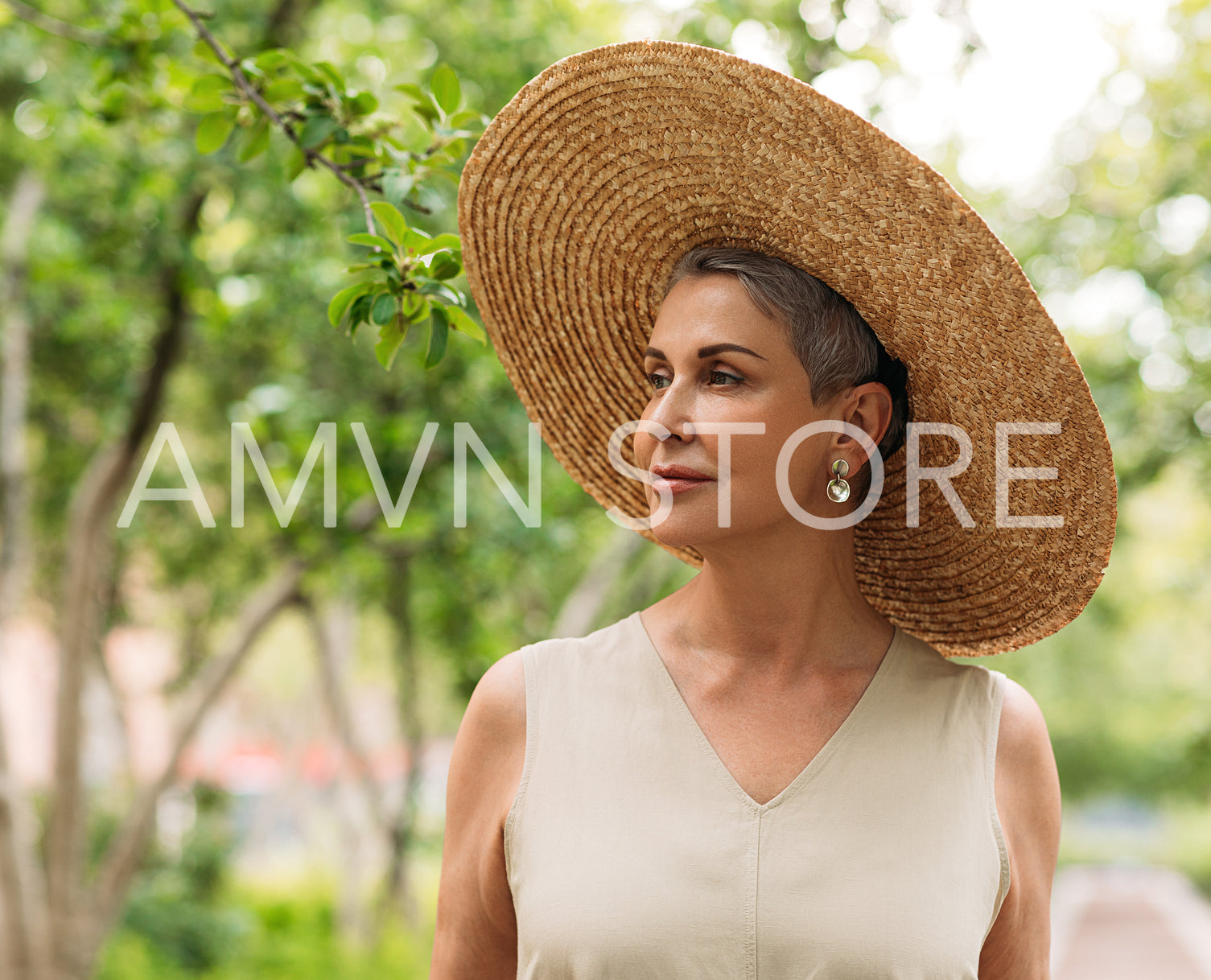 Portrait of an aged woman in a straw hat standing in the park at summer