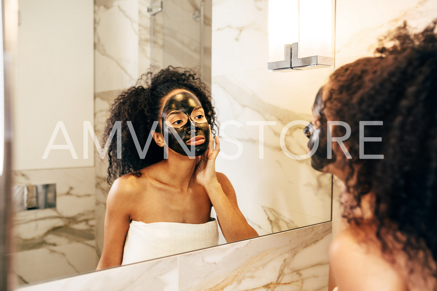 Beautiful woman in bathroom in front of a mirror with black natural mask	