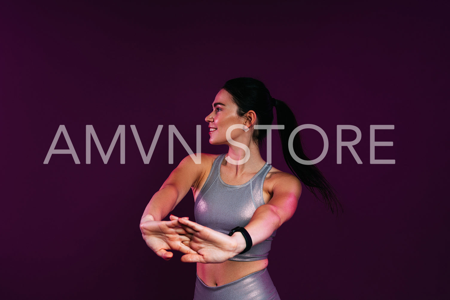 Slim woman in silver fitness wear doing warming-up exercises against a magenta background