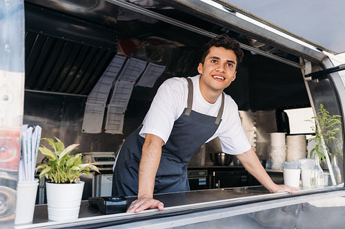 Young food truck owner in apron. Salesman looking away.