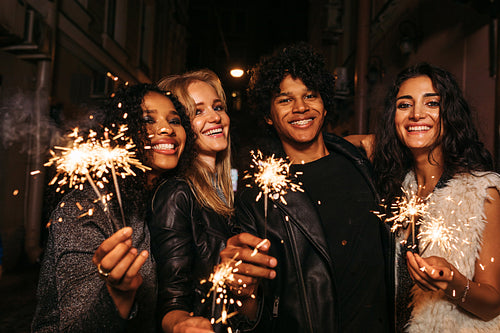 Four young friends celebrating new years eve with sparklers, standing together on street