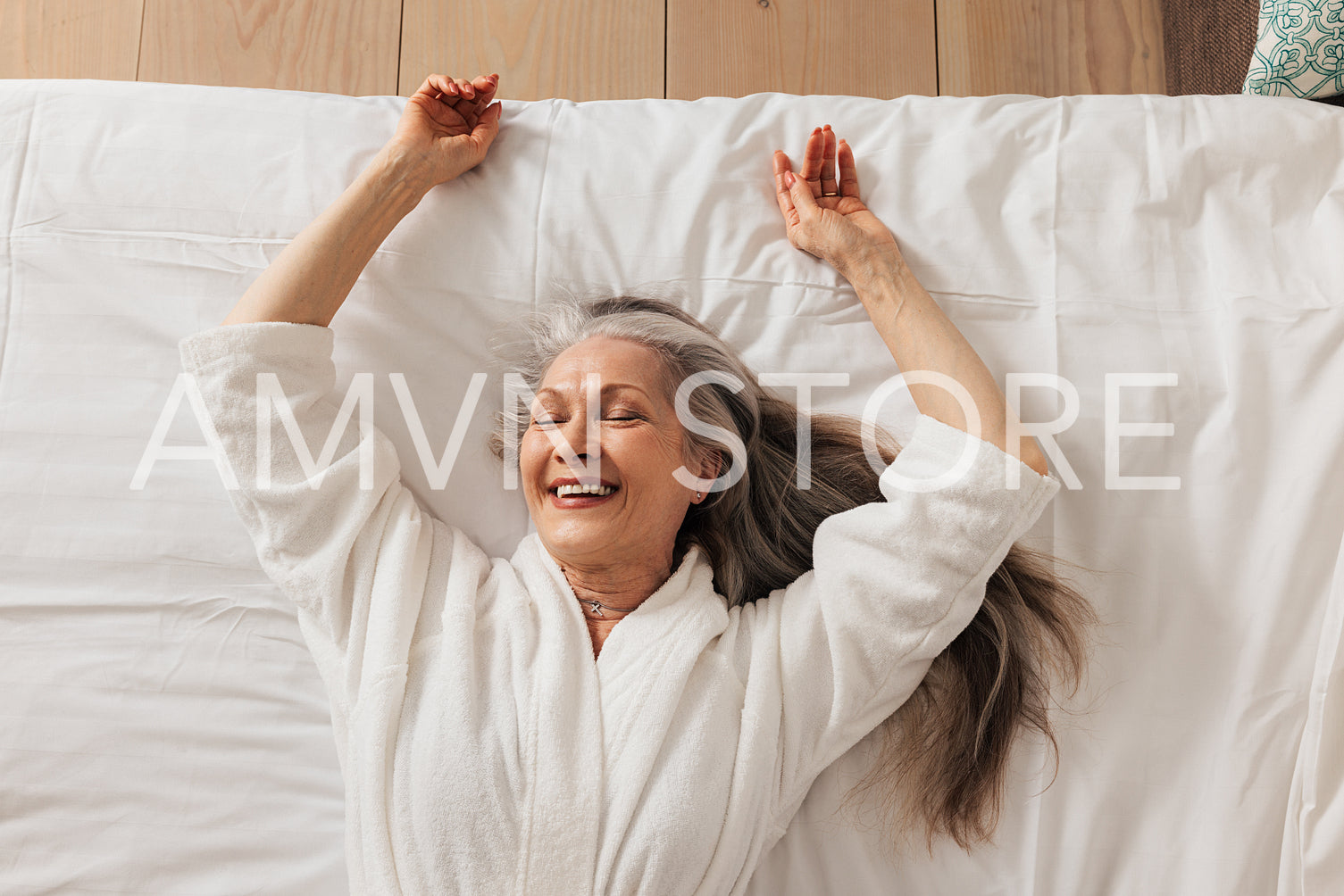 Happy aged woman in a bathrobe lying on a bed with closed eyes