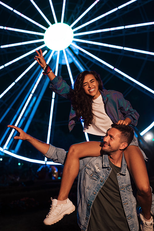 Happy couple having fun at night against lights of ferris wheel