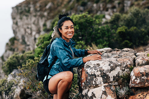 Smiling woman hiker in sports clothes taking a break and looking away during climbing