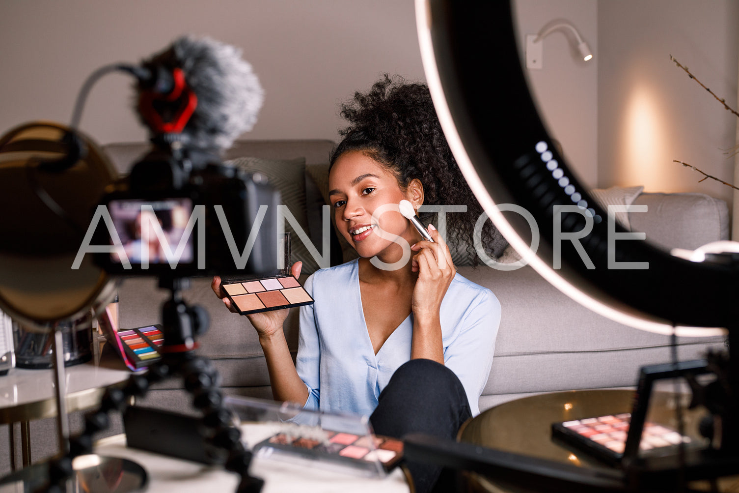 Smiling beauty blogger sitting in front of dslr camera with skin palette and brush in hands	