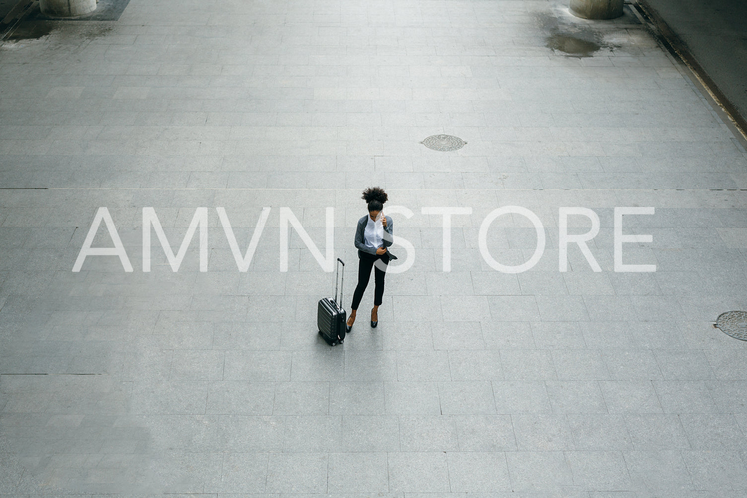 High angle view of young businesswoman standing at airport terminal with a suitcase and talking on mobile phone.	