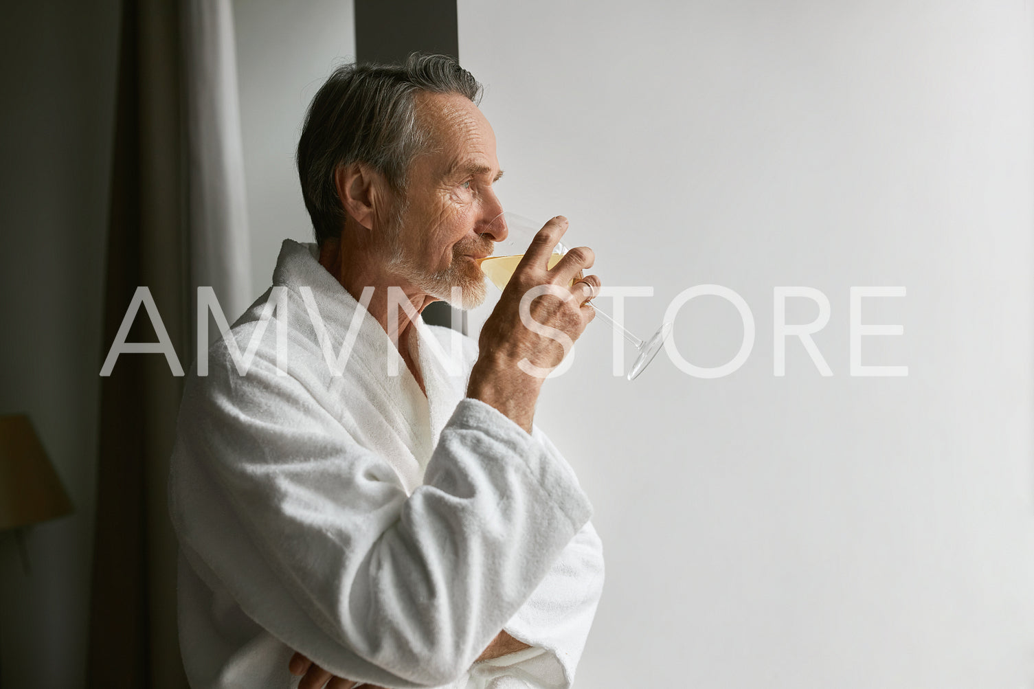 Side view of an elderly man drinking wine while looking at window in living room	