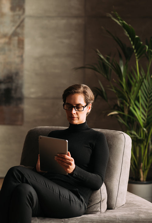 Businesswoman in black formal wear using digital tablet while sitting in her loft