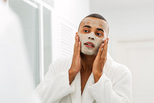 Man looking in the mirror with white clay mask on his face