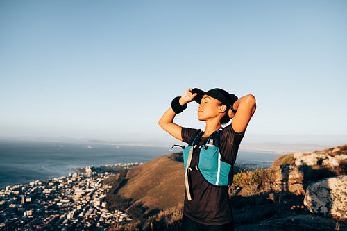 Woman hiker adjusting cap with closed eyes. Female trail runner feeling taking rest during a hike.