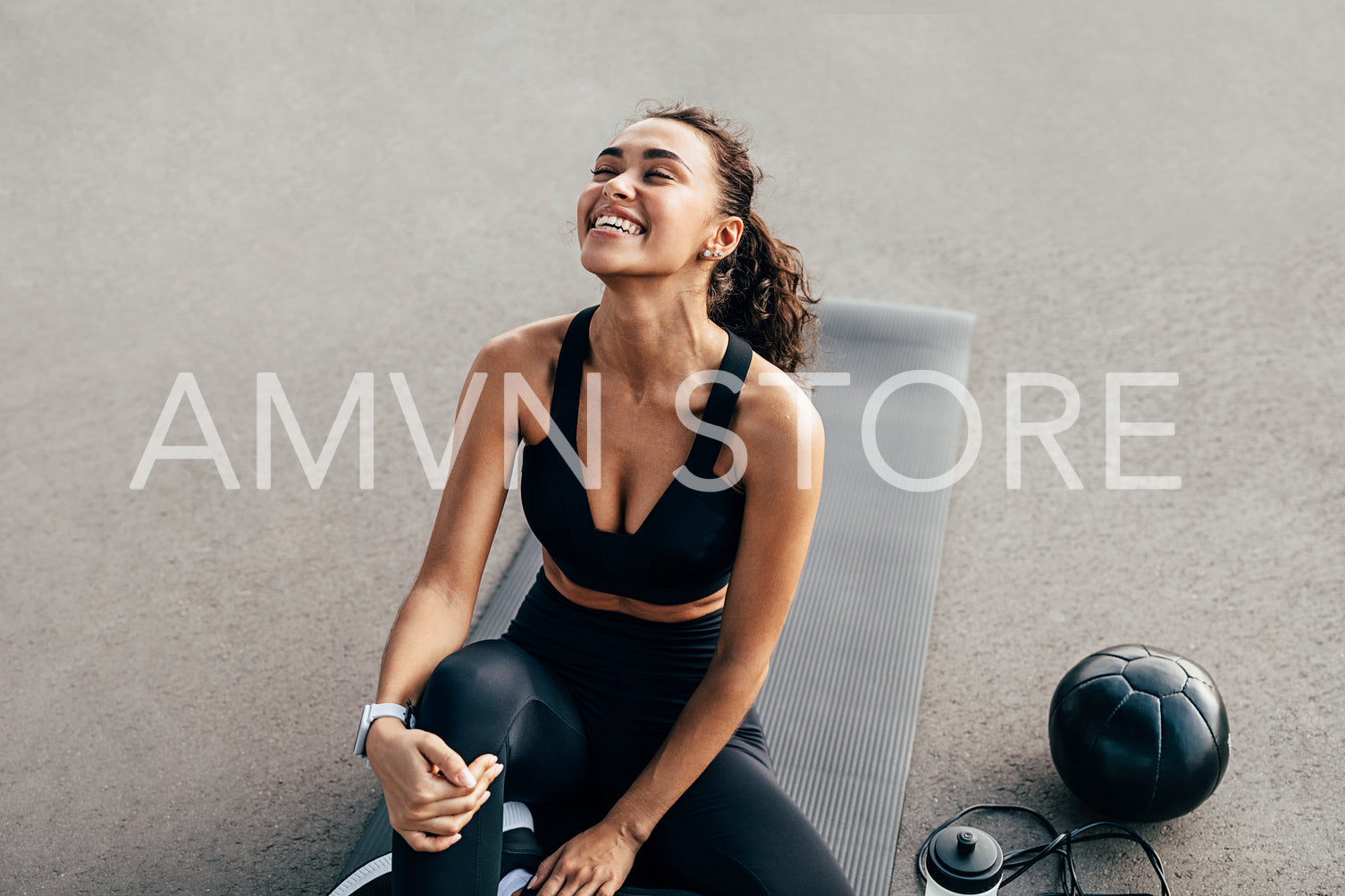 Laughing sport woman sitting on a mat with closed eyes	