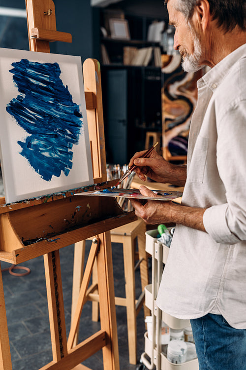 Senior painter standing in front of easel holding a paintbrush and palette