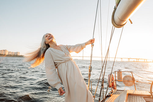 Happy senior woman wearing dress holding a rope on yacht