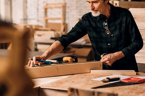 Carpenter measuring wooden plank with tape measure in workshop