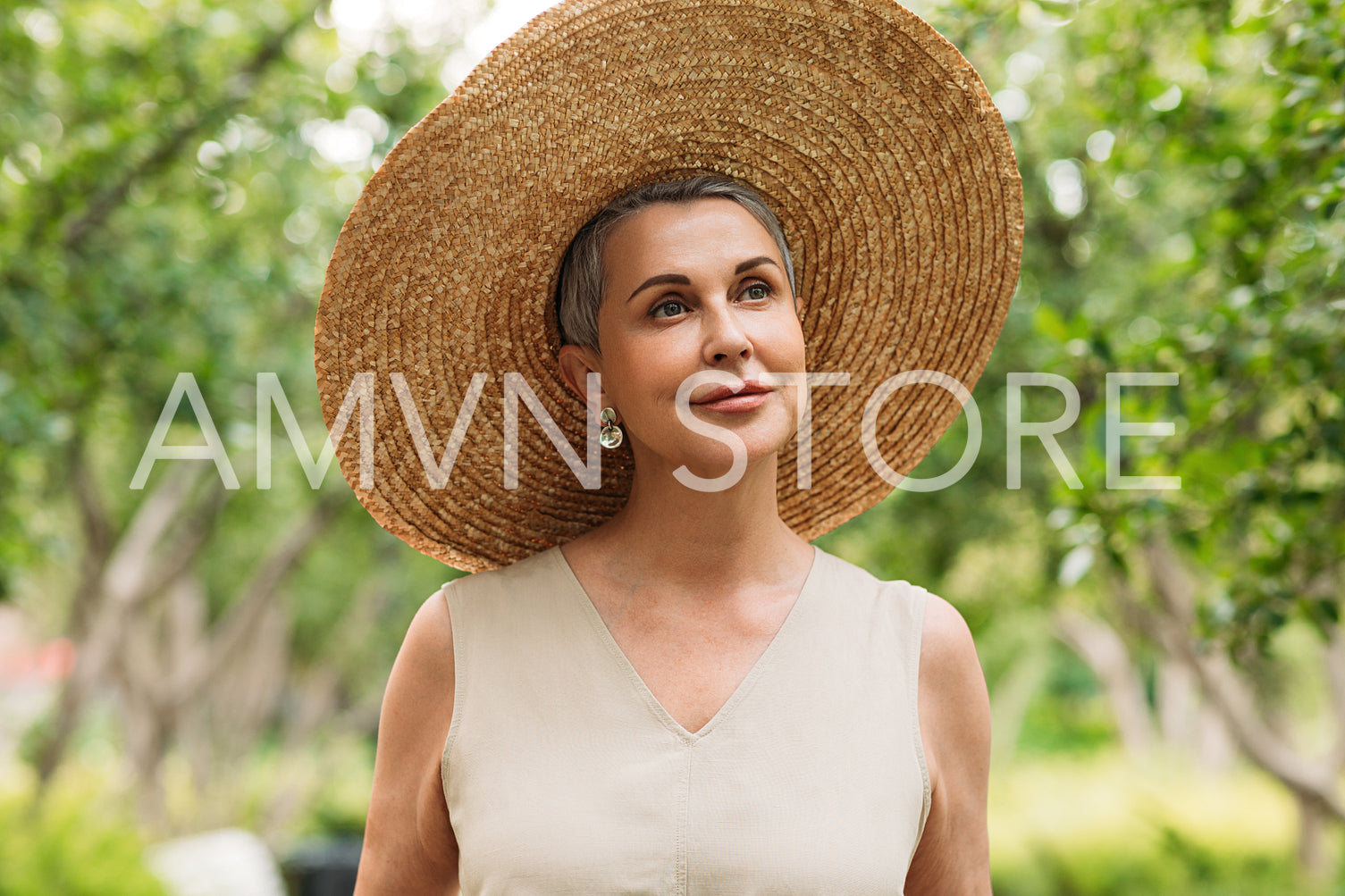 Aged woman with short grey hair wearing a straw hat walking in a park