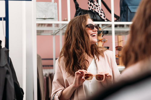 Happy woman looking away while choosing sunglasses in a fashion