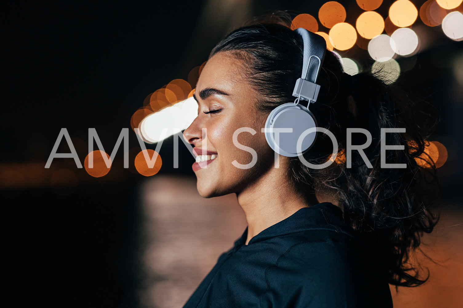 Close up of smiling woman in headphones standing against night city lights