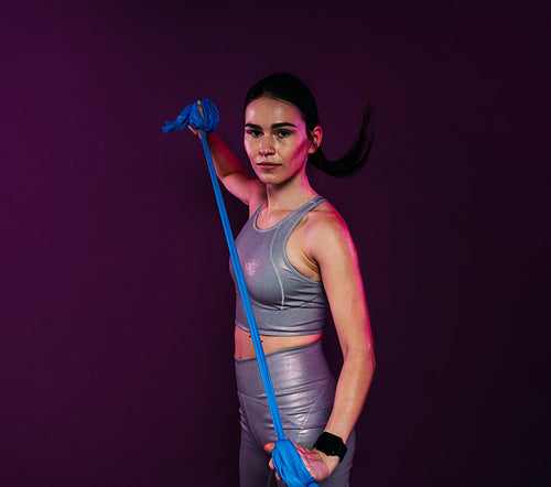 Confident sportswoman in silver fitness attire stretching her hands against a magenta background