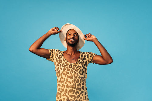 Smiling stylish man holding his straw hat and looking up against the blue background