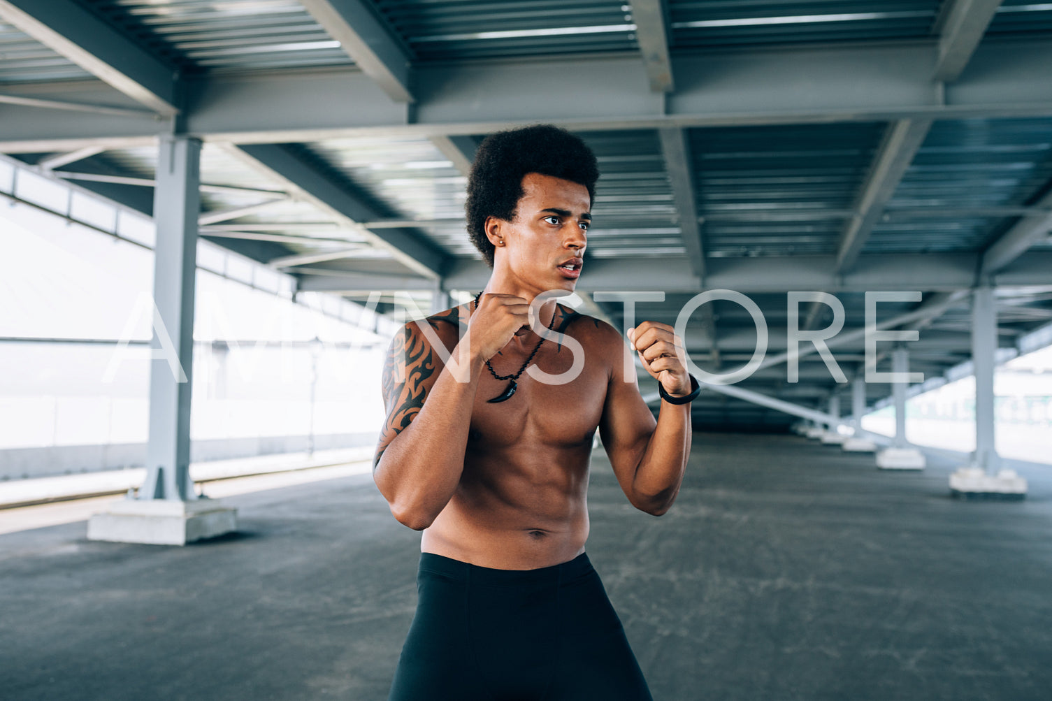 Bare chested kickboxer standing with raised fists under a bridge	