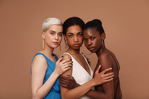 Three diverse women looking at camera. Young females with different skin tones standing together.