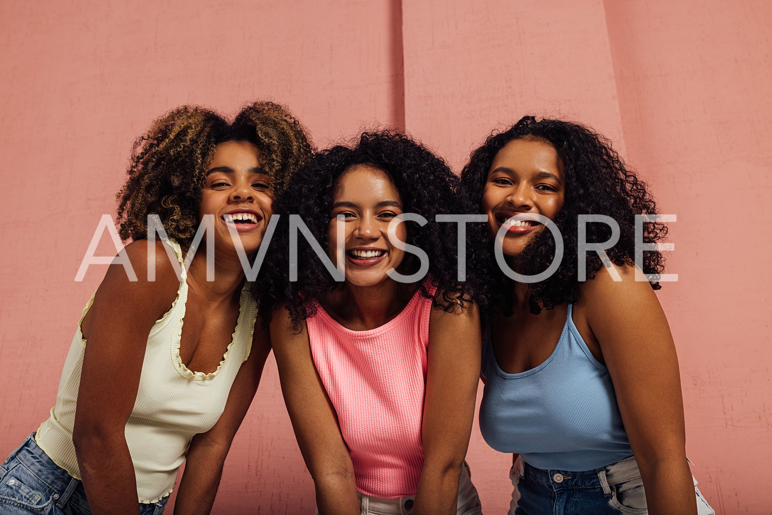 Three happy girls with curly hair standing together and looking at camera