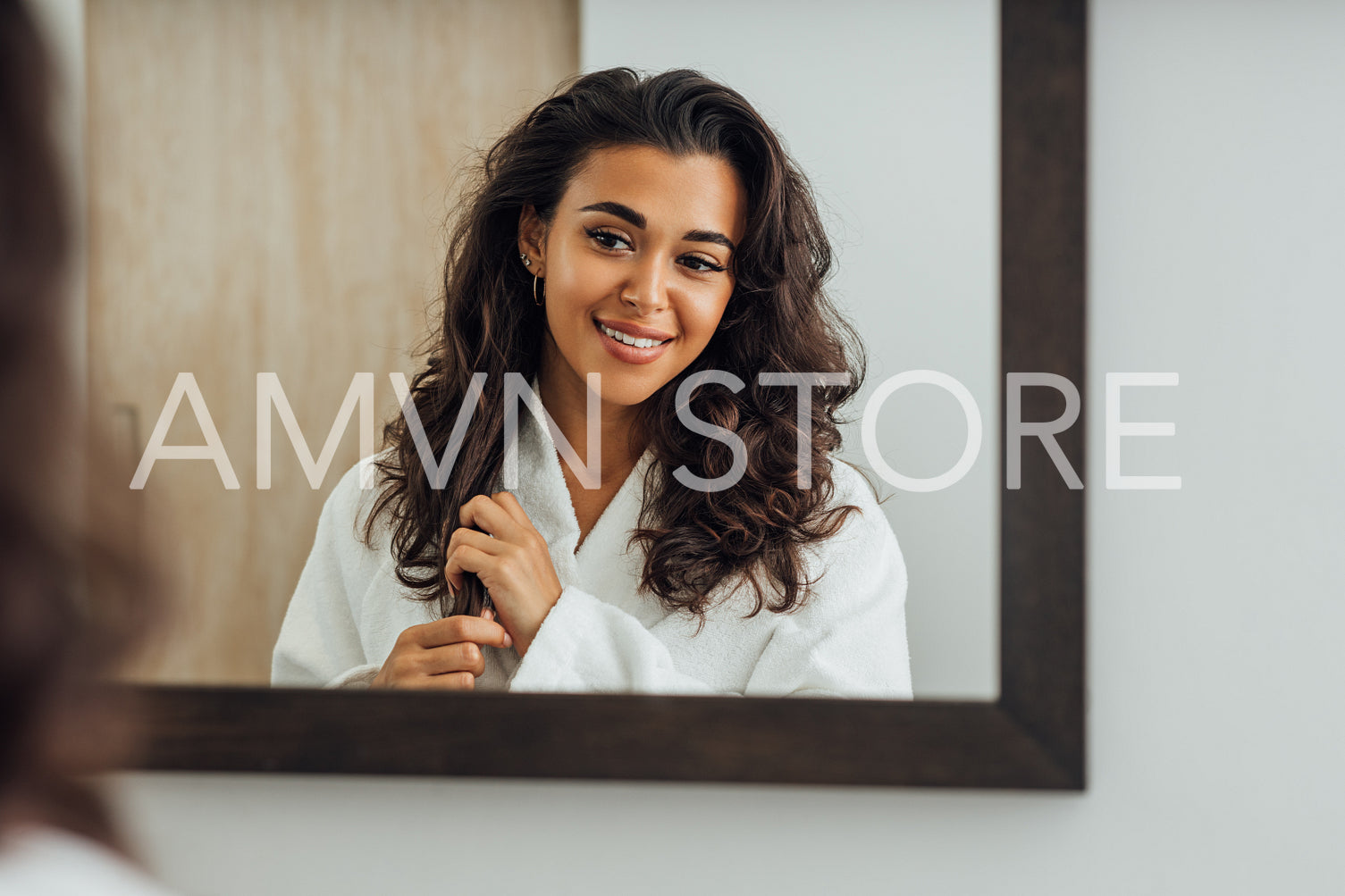 Reflection of a brunette woman in bathroom mirror touching hair	