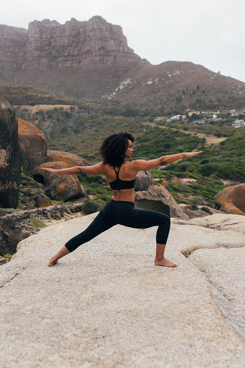 Female in sportswear practicing yoga outdoors. Fit woman doing warrior pose against landscape.