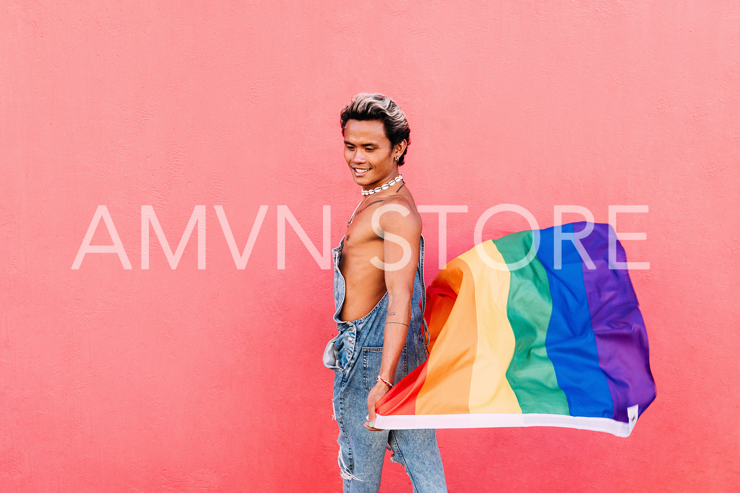 Side view of a young stylish guy walking with rainbow flag at pink wall