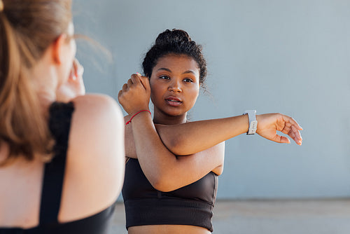 Female with curly hair stretching her hand before training while standing outdoors with her friend