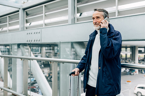 Senior tourist standing in airport terminal and talking on mobile phone