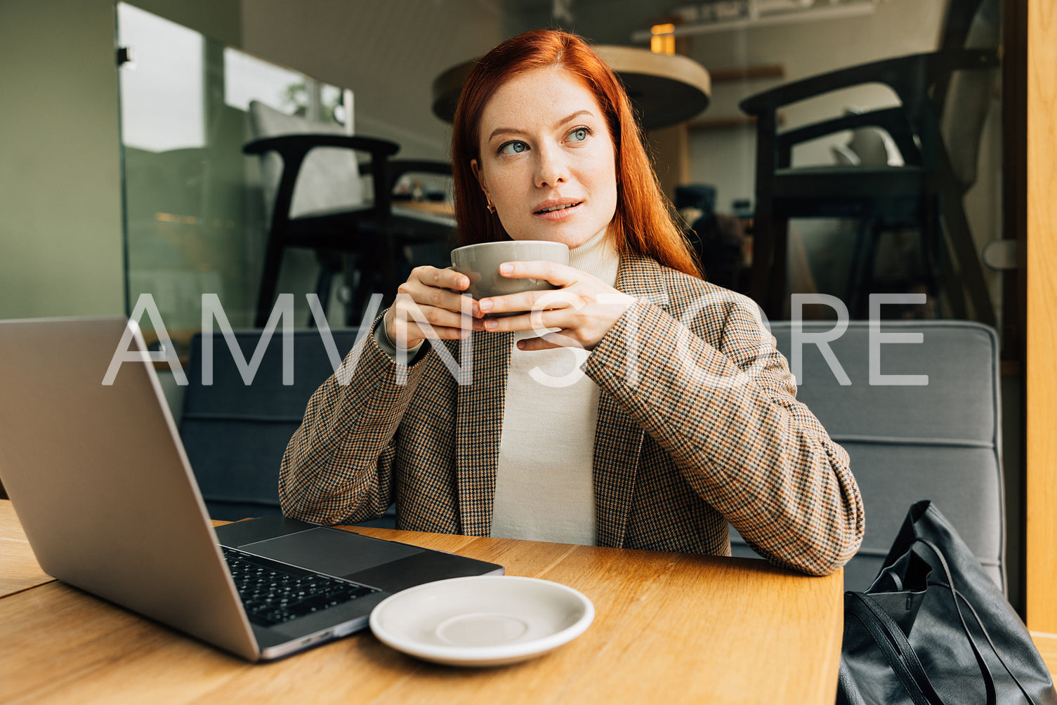 Woman with ginger hair holding a cup and looking at the window at a cafe. Businesswoman enjoying her coffee.