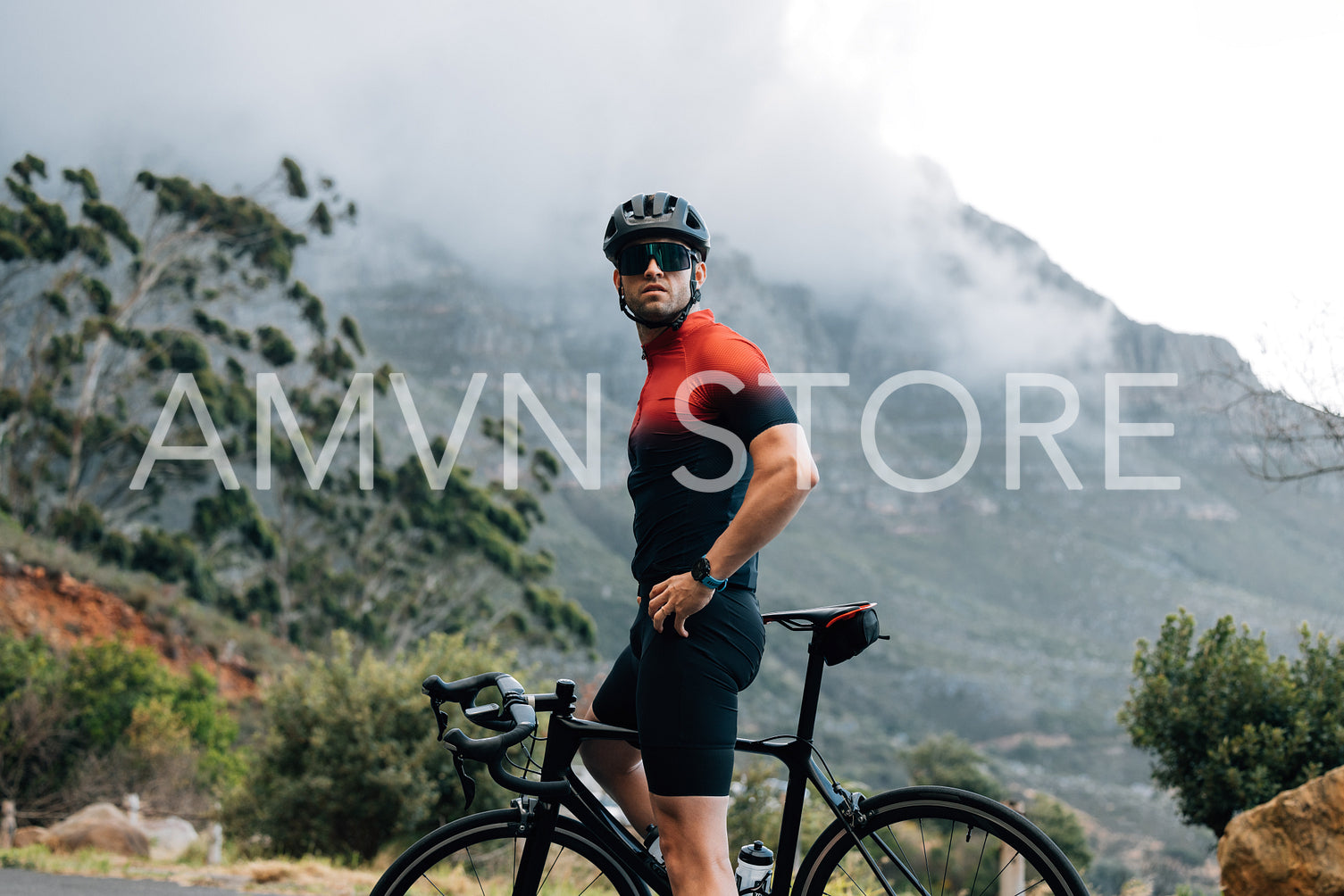 Male cyclist relaxing during his outdoor ride. Cyclist wearing helmet and glasses with bike against mountain looking away.