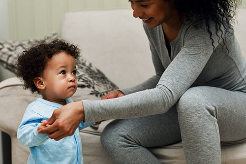 Young mother holding her child hands in living room. Toddler looking at camera.