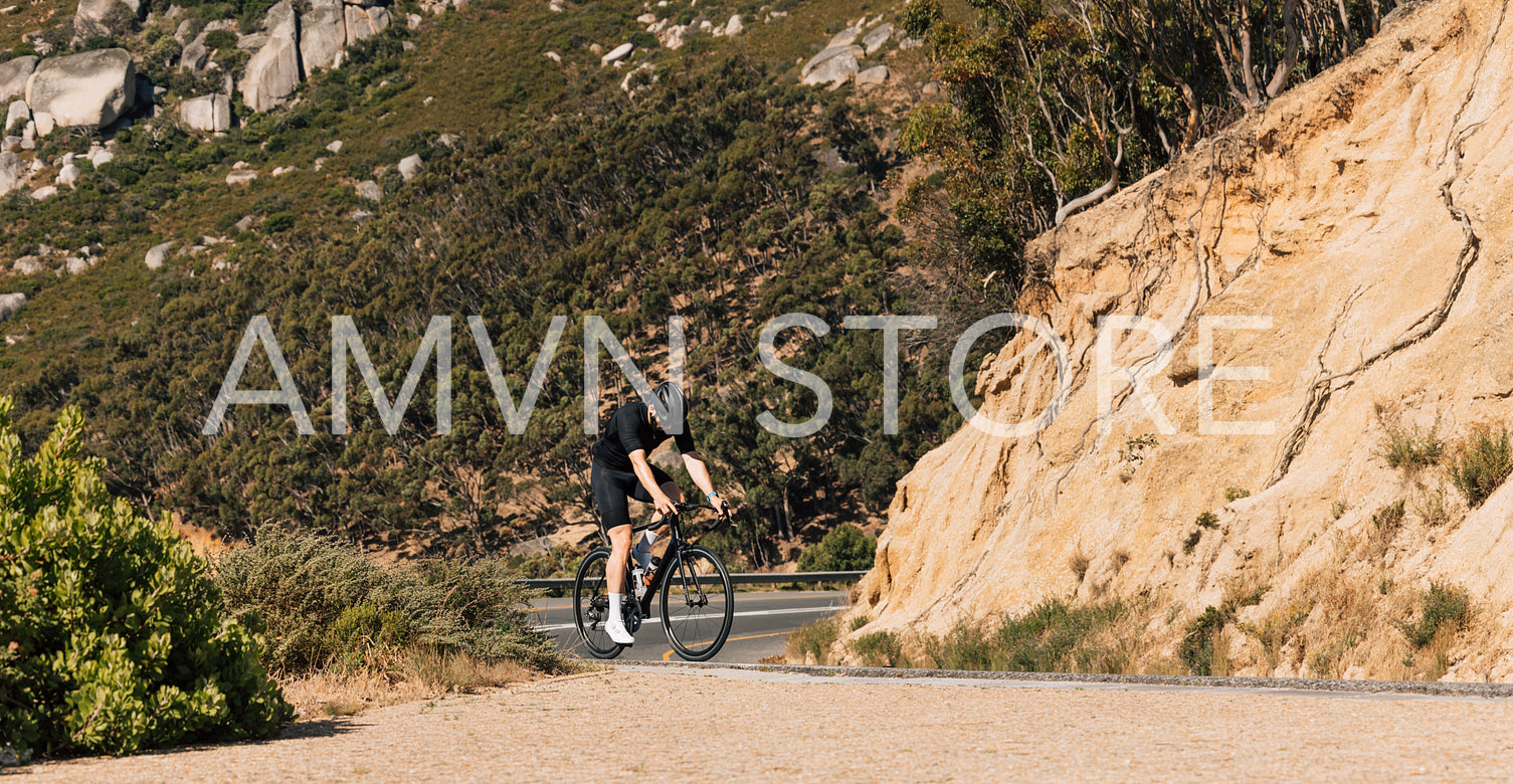 Young male cyclist practicing on an empty road in wild terrain