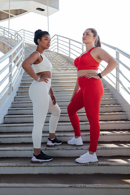 Full length of two plus size females wearing sportswear with different colors. Young women relaxing after exercising outdoor.