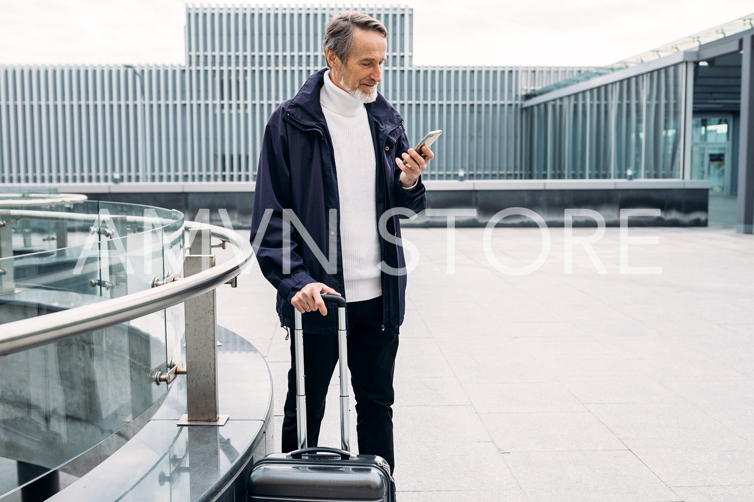 Senior businessman standing outdoors with suitcase and looking on smartphone	