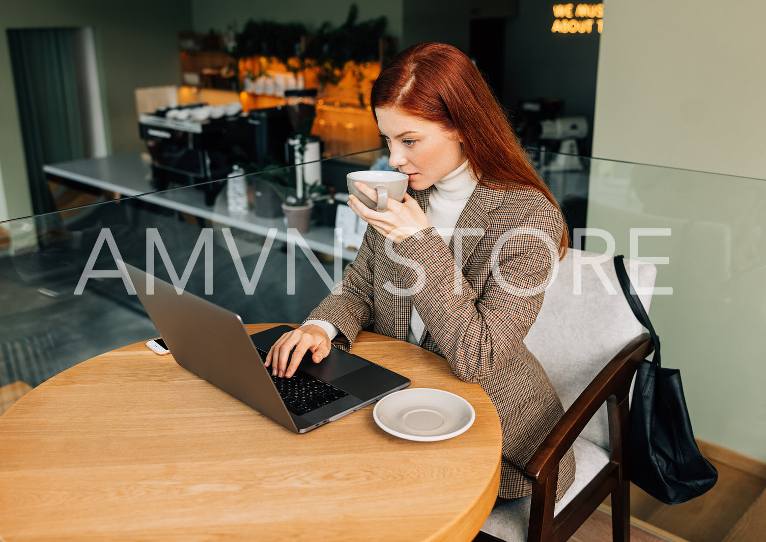 Young female entrepreneur with ginger hair typing on a laptop and drinking coffee at a cafe