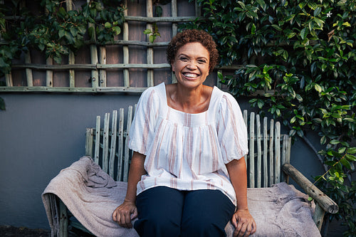 Happy mature woman on a bench. Smiling woman with short hair relaxing in backyard.