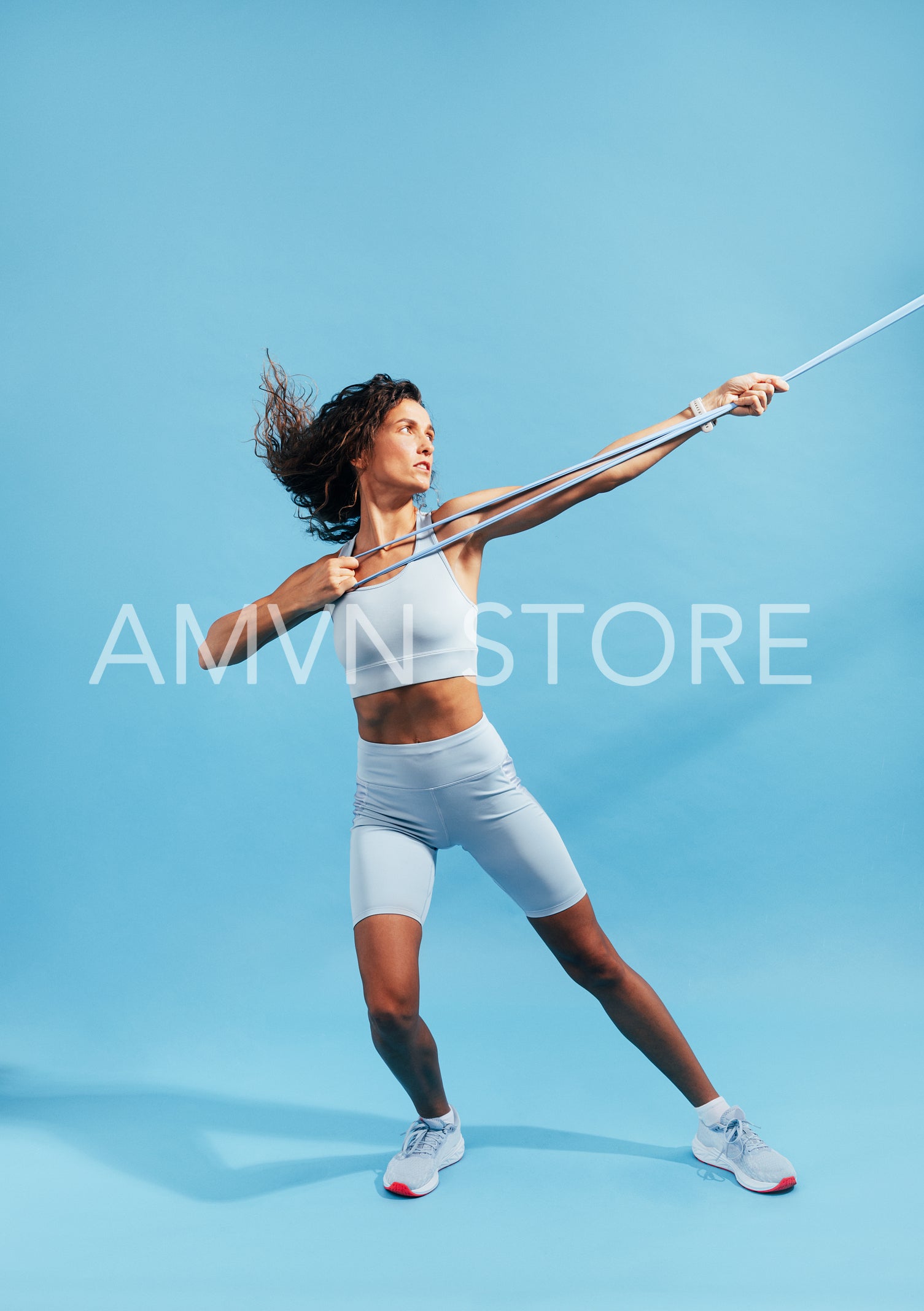 Full length of a slim woman in sportswear practicing on blue background with a resistance band