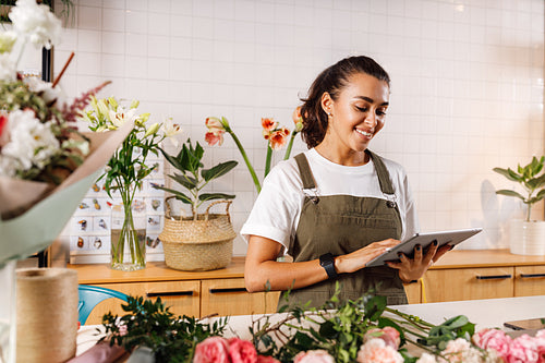 Young female florist making notes on a digital tablet. Woman checking online orders in shop.