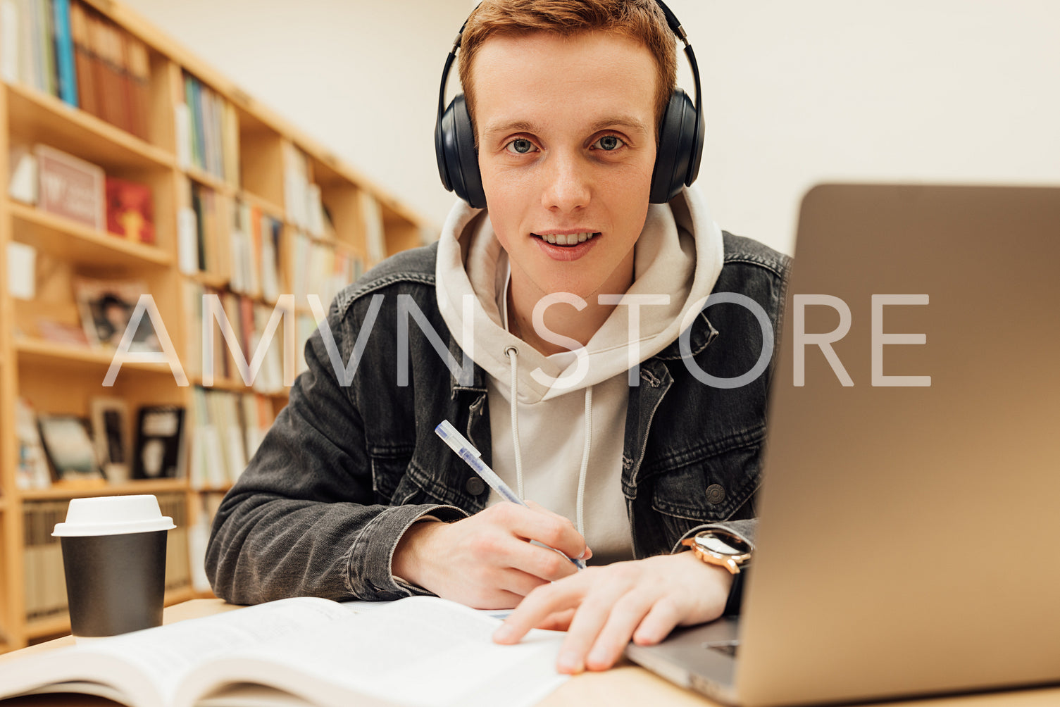 Smiling student in headphones holding pen sitting at desk looking at camera